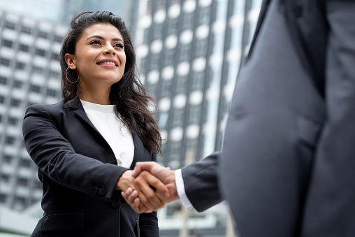 Young smiling Hispanic businesswoman making handshake with partner in the city for greeting, dealing, merger and acquisition concepts