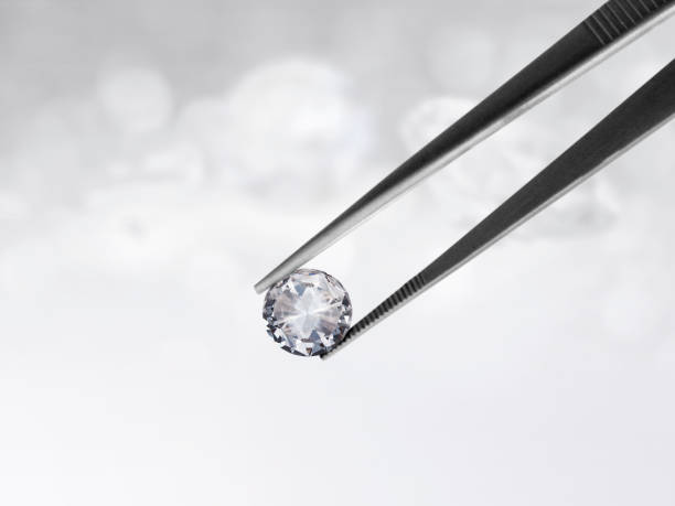 istock Diamond in tweezers on white shining bokeh background. concept for chossing best diamond gem design 1354526245