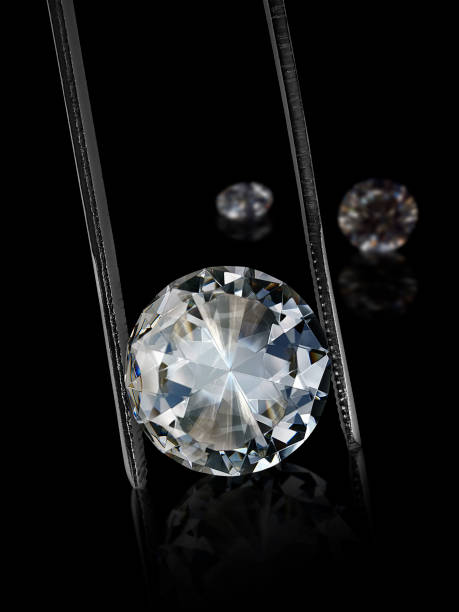 istock Diamond in tweezers on a black background with diamonds group soft focusing 1354527007