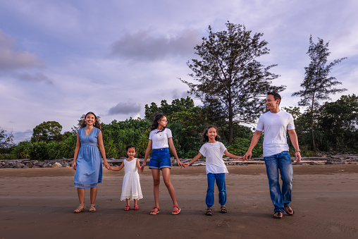 family, leisure and people concept-young active parents with three daughters with arms up, enjoying summer vacation together. Big asian happy family of five.