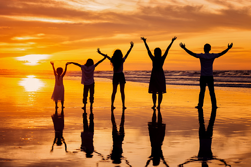 vista trasera silueta de familia feliz tomados de la mano y divirtiéndose juntos en la playa tropical al atardecer de verano photo