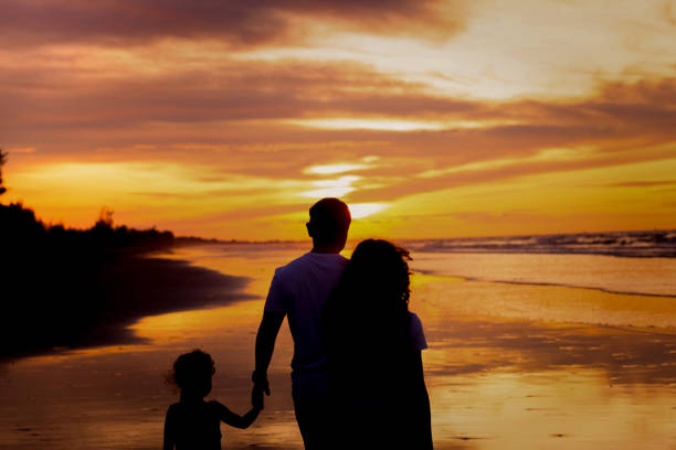 istock Silhouettes of happy father with two daughters on beach during sunset 1354530139