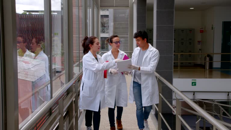 Group of Latin American medical students walking through the university hallway discussing their notes all wearing lab coats and protective gloves