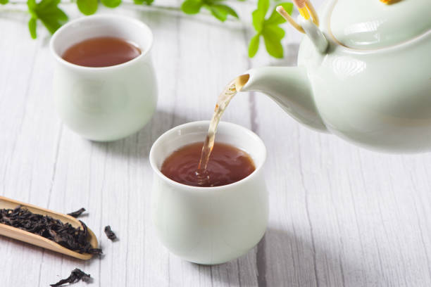 istock Pouring black tea into glass cup on wooden table 1354534541