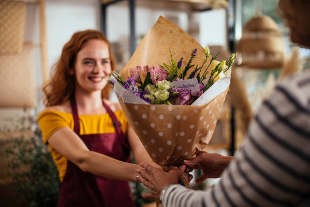 Thanks for visiting us Young redhead woman giving her customer a beautiful bouquet of flowers bunch of flowers stock pictures, royalty-free photos & images