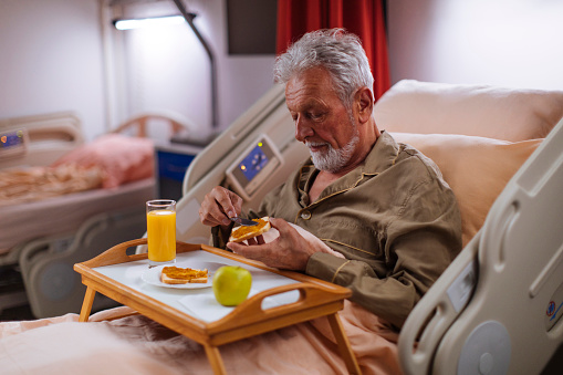 Senior man having breakfast while lying in a hospital bed