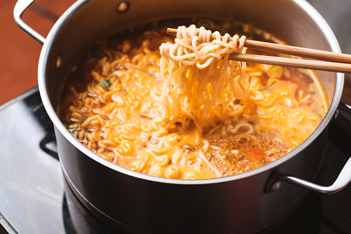 Asian spicy instant noodles soup cooking in hot pot with chopsticks, Close up
