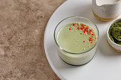Matcha panna cotta dessert with confectionery decor in a glass on a white tray and beige background. Minimalistic and warm photography.