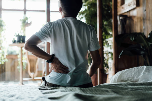 istock Rear view of senior Asian man suffering from backache, massaging aching muscles while sitting on bed. Elderly and health issues concept 1354565582