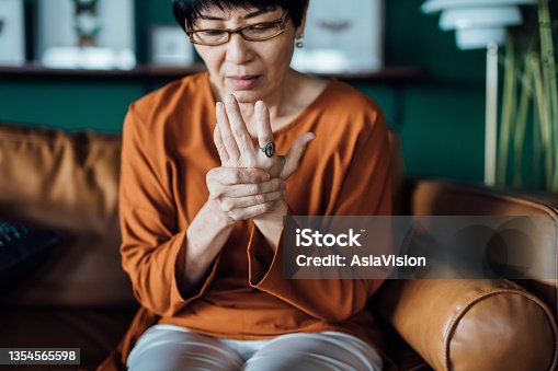 istock Senior Asian woman rubbing her hands in discomfort, suffering from arthritis in her hand while sitting on sofa at home. Elderly and health issues concept 1354565598