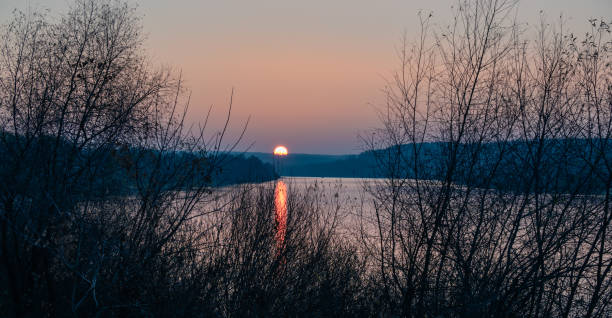 istock Sun sets beyond the horizon with reflections on the river surface in autumn. 1354567683
