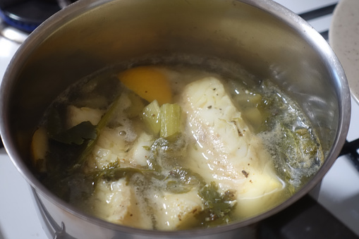 Cod fillet being cooked in a court-bouillon with lemon, celery and spices