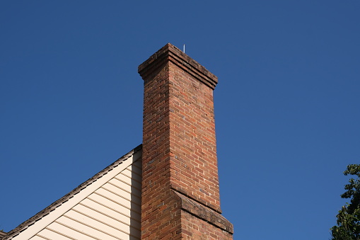 Smoke rises from the chimney on the house. Roof with smoking chimney and trees in winter. High quality photo