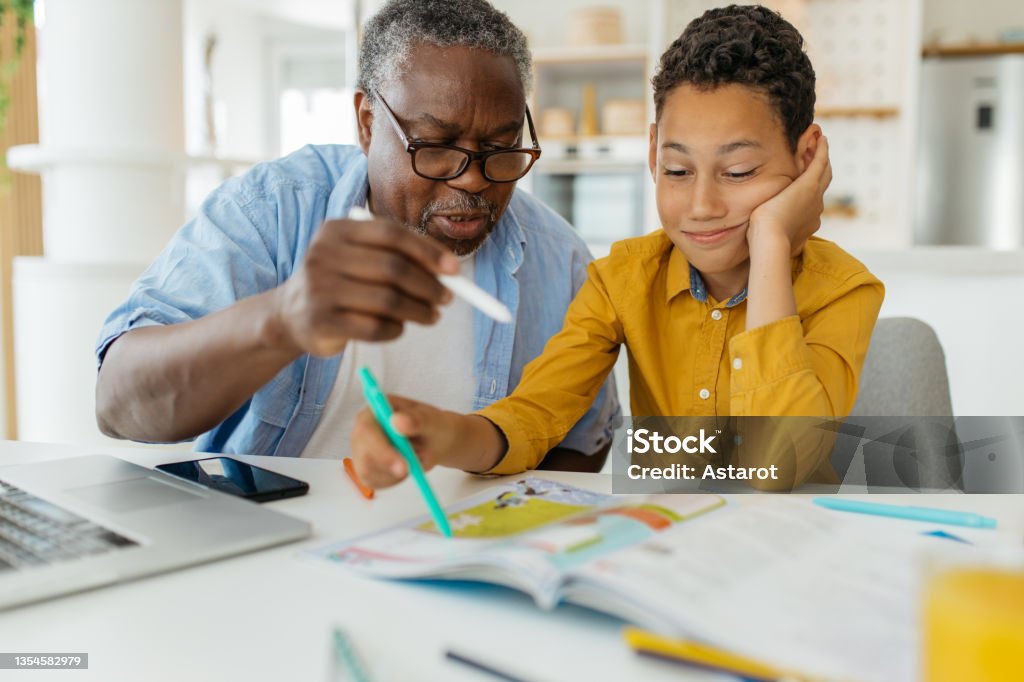Grandfather tutoring his grandson at home Grandfather tutoring his grandson at home. The child is patiently listening and learning while grandad showing him how to solve the problem. Tutor Stock Photo