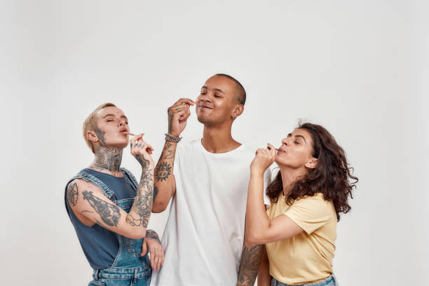 jóvenes diversos divirtiéndose juntos, comiendo coloridos caramelos de gusano gomoso de azúcar agria, de pie aislados sobre un fondo gris - tasting women eating expressing positivity fotografías e imágenes de stock