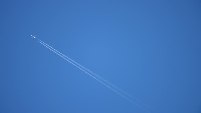 Aircraft gliding in a blue sky filling two white streaks of dense smoke in summer