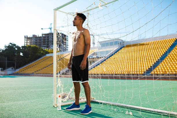 jovem jovem atleta afro-americano sem camisa sem camisa está perto do gol de futebol no estádio da cidade - football player - fotografias e filmes do acervo