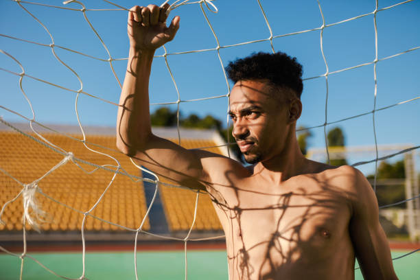 retrato de um atraente esportista afro-americano sem camisa, pensativo, olhando para o gol de futebol no estádio da cidade - football player - fotografias e filmes do acervo