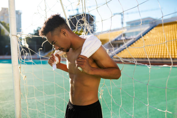 confiante desportista afro-americano sem camisa com toalha nos ombros após jogo de futebol no estádio da cidade - football player - fotografias e filmes do acervo