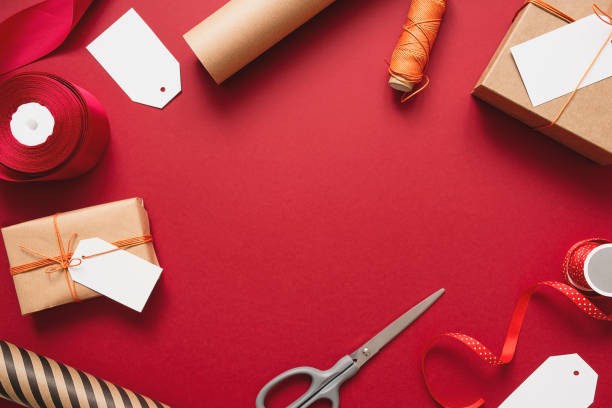 istock Kraft gift boxes with orange thread on a red background. Packaging and preparation of gifts for the celebration. 1354612194