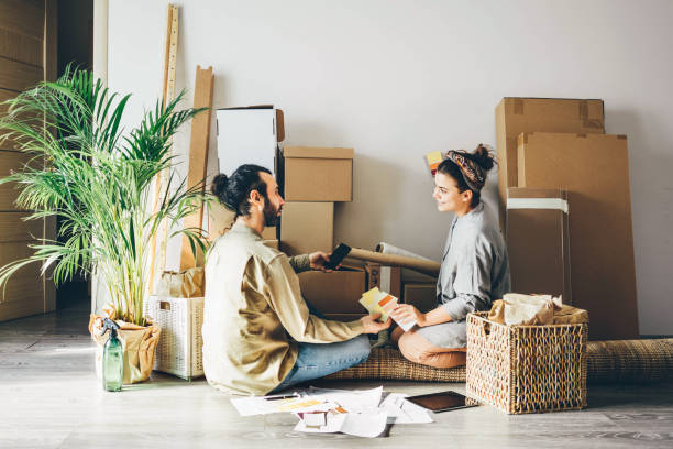 hombre y mujer jóvenes alegres que usan ropa casual eligen el mejor color para la nueva pared espaciosa del apartamento sentada en el piso cerca de una pila de cajas. - moving house physical activity real estate couple fotografías e imágenes de stock