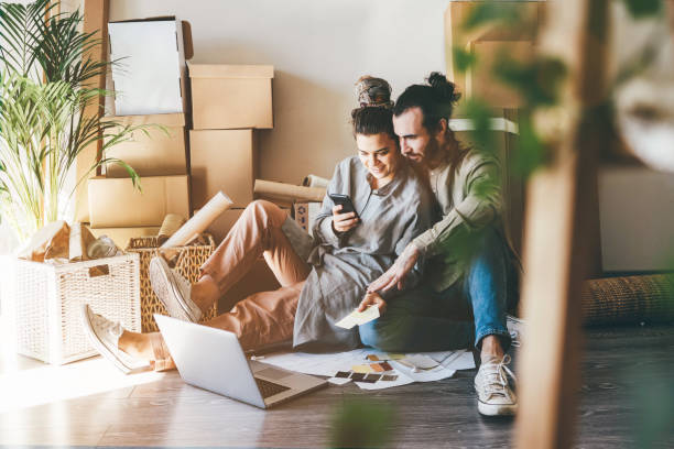 alegre familia joven de hombre y mujer con ropa casual hace proyecto de decoración para nuevo apartamento en computadora portátil sentado en el piso cerca de la pila de cajas - moving house physical activity real estate couple fotografías e imágenes de stock