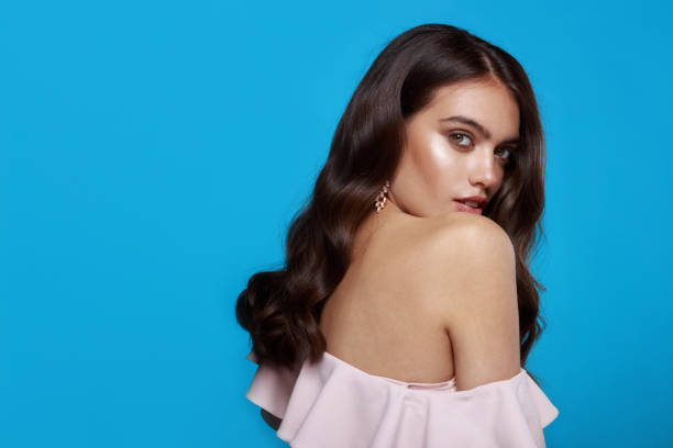 istock Sensual model, hairstyle and makeup, dressed in pink blouse whith bare shoulder, over blue background. 1354614610