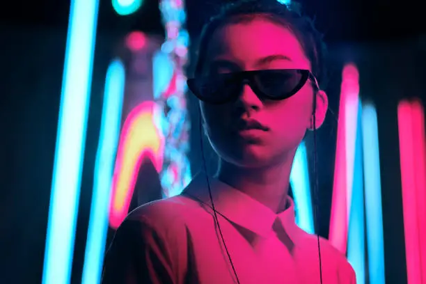 Portrait of young asian teenage girl in stylish crescent shaped sun glasses, in red anf blue neon light. Cyber, futuristic portrait concept