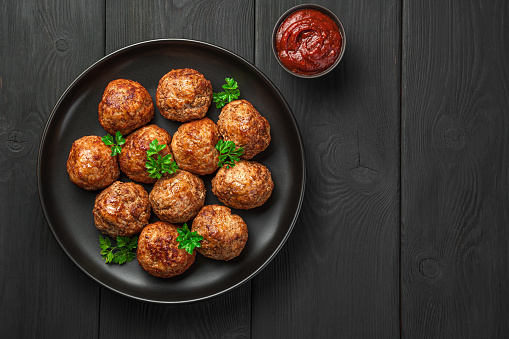 Meatballs with basil and tomato sauce on a black background. Top view, copy space.