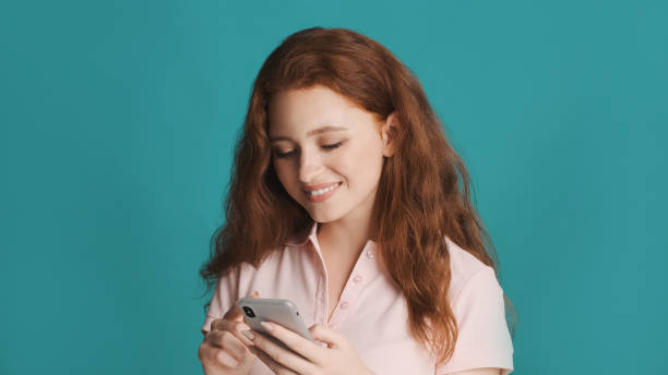 istock Pretty smiling redhead girl happily using smartphone over colorful background 1354620530