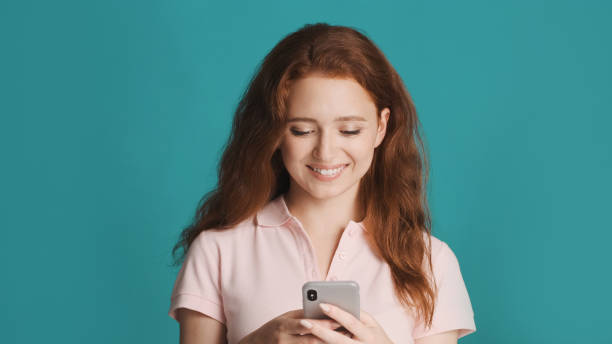 istock Beautiful smiling redhead girl happily using smartphone on camera over colorful background 1354620538
