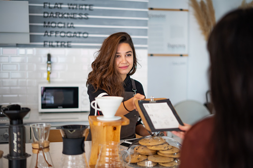 Female barista smiles at the customer and giving her the menu.