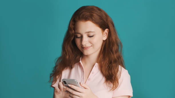 istock Beautiful smiling redhead girl intently using smartphone over colorful background 1354626878