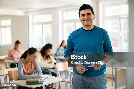 istock Portrait of happy high school teacher in the classroom looking at camera. 1354640844
