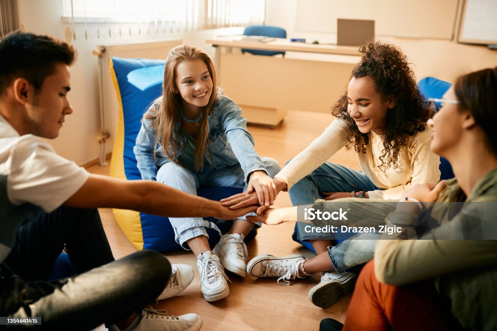 Happy high school students gathering their hands in unity during a break in the classroom. Multiracial group of teenagers uniting hands while celebrating their friendship in the classroom. Teenagers Only Stock Photo