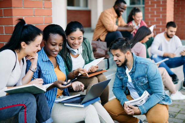 Multiracial group of university students e-learning on laptop at campus. Multi-ethnic group of happy college friends surfing the net on laptop at campus. campus stock pictures, royalty-free photos & images