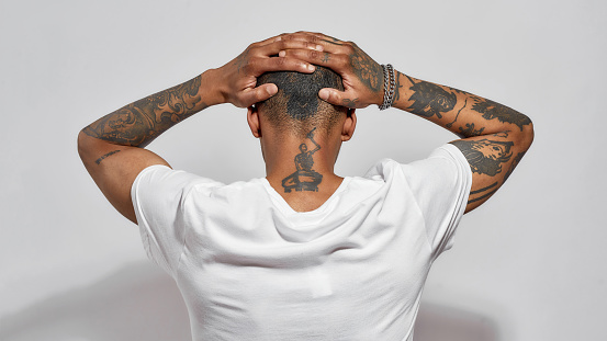Back view of tattooed head, neck and arms of young dark skinned man posing isolated over white background. Web Banner