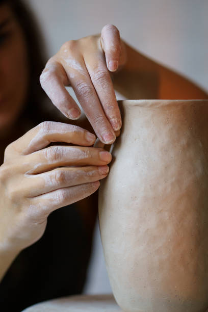 istock Craftsmanship: female artisan working with wet clay decorating shaping jug in pottery studio space 1354642572