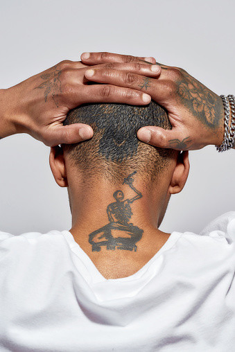 Bac view of shaved tattooed head and neck of young dark skinned man posing isolated over white background. Vertical shot