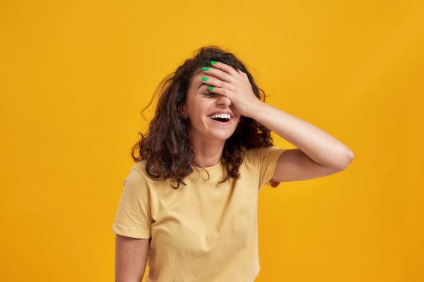 Portrait of woman with curly dark hair forgetting something, slapping forehead with palm and closing eyes isolated over yellow background stock photo