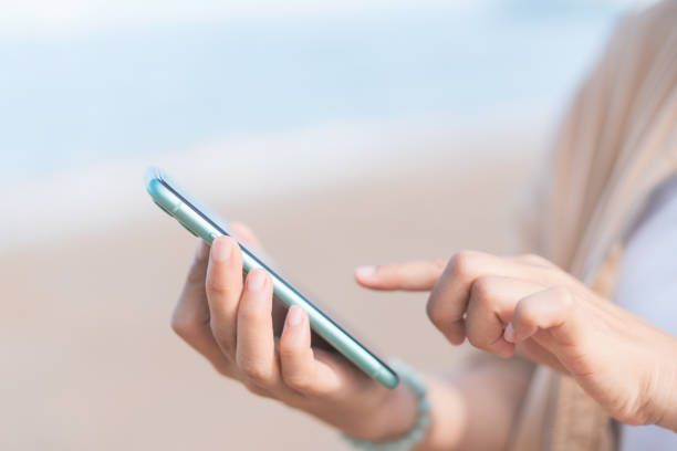 istock Woman hand using smart phone on tropical beach abstract background. 1354660456