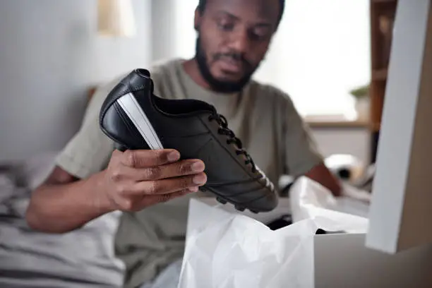 Hands of young African man with black sports-shoe putting it into bag or unpacking box with sporty footwear