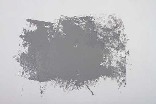 A gray spot of paint is painted on a white wall, a bizarre relief shape of the blob is applied with a roller on a white surface. Background. Copy Space.