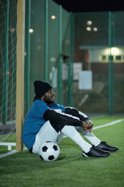 istock Young restful football player sitting by net after hard training 1354672325