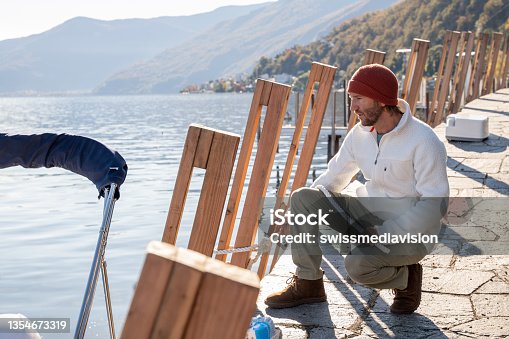 istock Young man docking boat on lake in Autumn 1354673319