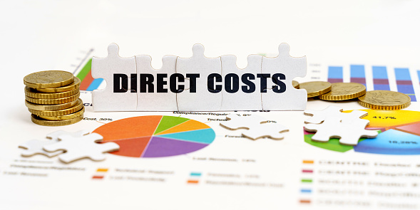 Business and Economics. There are coins and puzzles on financial charts with the inscription - DIRECT COSTS