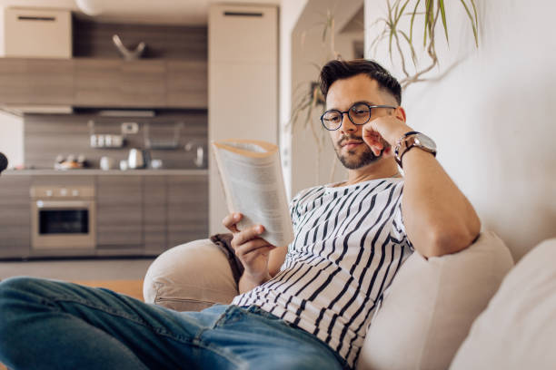 istock Young man sitting on the sofa and reading a novel 1354681694