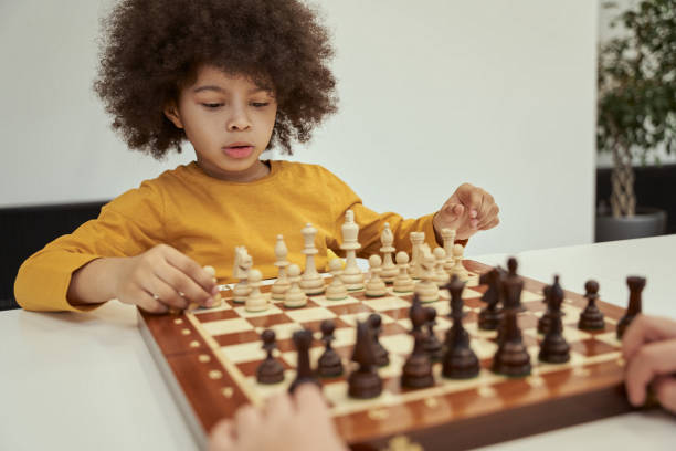 istock Cute little boy with afro hair thinking before making a move while playing chess, sitting at the table indoors 1354688171