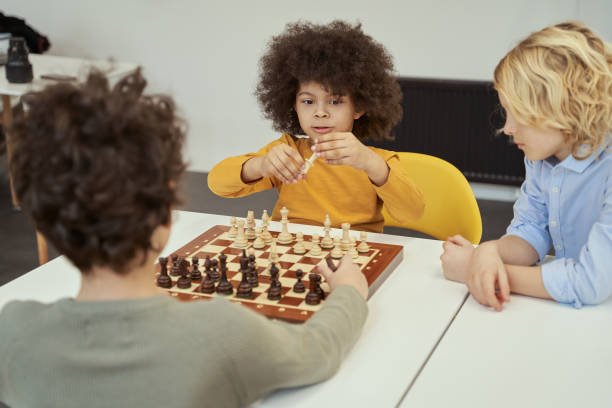 istock Holding piece. Awesome little boys discussing game while sitting at the table and playing chess indoors 1354688185