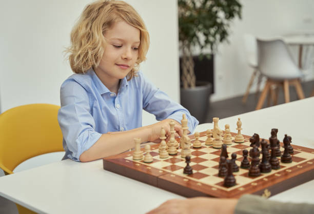 istock Smart little boy in blue shirt sitting in the classroom, looking at the chessboard while playing chess 1354688200